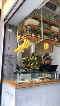 a man working at a counter with bananas hanging from the ceiling and shelves above him