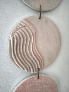 two circular objects hanging from hooks on a white wall, one with wavy lines and the other with curved shapes