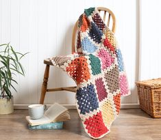 a crocheted blanket sitting on top of a wooden chair next to a book