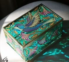 a decorative box sitting on top of a white tablecloth covered table with green and blue designs