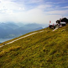 a person standing on top of a grass covered hill next to a lake and mountains