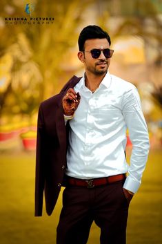 a man in a white shirt and maroon pants is posing for the camera with his hand on his hip