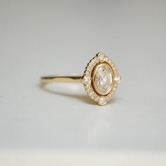 a yellow gold ring with an oval cut diamond surrounded by small white diamonds