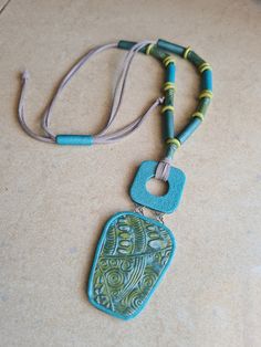 a blue and green beaded necklace on a beige surface with a brown leather cord