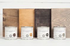 three cans of paint sitting on top of a white shelf next to wooden planks