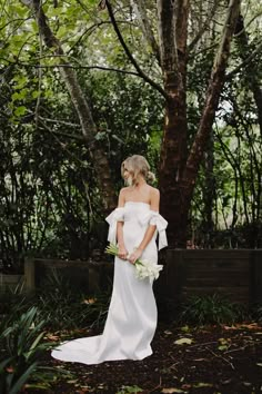 a woman in a white dress standing next to a tree with her hands on her hips