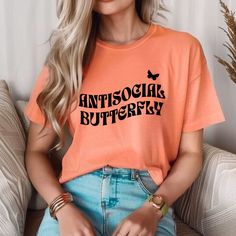 a woman sitting on a couch wearing an orange shirt with the words antsogra butterfly