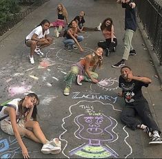 a group of young people sitting on the side of a road next to chalk drawings