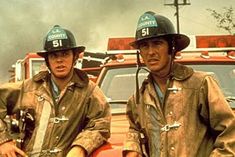 two firemen standing next to each other in front of a truck