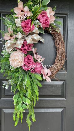 a wreath with pink and green flowers hanging on the front door, decorated with greenery