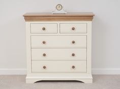 a white dresser with two drawers and a clock on it's top, against a wall