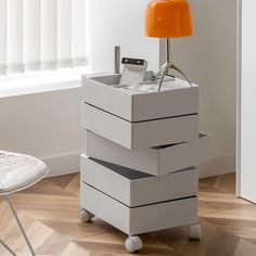 an orange lamp is sitting on top of a white box with four drawers in front of it