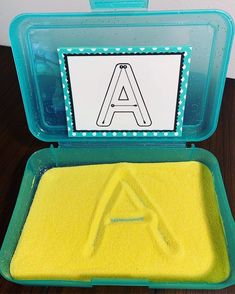 a plastic container filled with yellow sand next to a sign that says a is for a