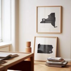 two framed black and white pictures on a wall next to a wooden table with books