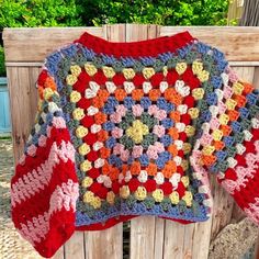 a crocheted sweater hanging on a wooden fence