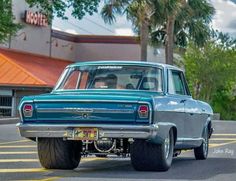 an old blue car driving down the street in front of a motel sign and palm trees