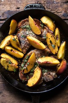 a skillet filled with meat and peaches on top of a wooden table