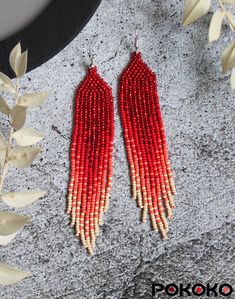 two pairs of red beaded earrings on top of a stone slab next to leaves