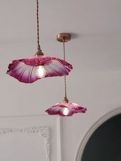 two pink lamps hanging from the ceiling in a room with white walls and flooring