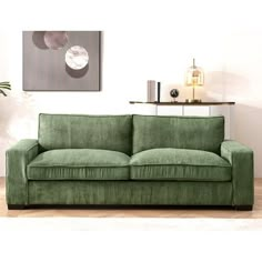 a green couch sitting in front of a painting on top of a wooden floor next to a white wall