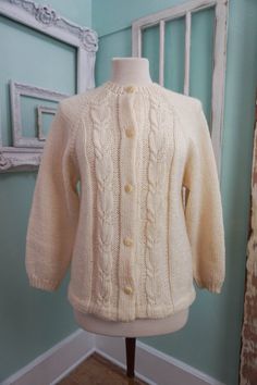 A classic women's cardigan sweater, in a soft ivory white acrylic. It has a unique wide pattern of traditional cable knit down the front. It closes up the front with a row of really unique swirly plastic buttons. The sweater is soft and comfy, not stiff at all. No damage or issues. Please check measurements carefully. Condition: Very Nice Vintage Tag: 100% Acrylic Size L Measurements in inches.... Length: 23.5 Chest: 19 ✩ Because you don't want to miss a thing, follow @heartkeyologie on Facebook Elegant Cream Cable Knit Cardigan, Elegant Cream Cable Knit Outerwear, Fitted Cream Knitted Outerwear, Fitted Cream Sweater With Buttons, Classic Hand Knitted Sweater For Winter, Classic Knit Cardigan For Winter, Elegant White Cable Knit Cardigan, Fitted Cream Knitted Sweater, Classic Fitted Knitted Cardigan