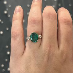 This rare and beautiful green emerald and diamond ring is perfect for any modern engagement! This oval cut emerald marquise diamond ring is finished in 14 karat yellow gold. Sleek modern in design. The center emerald reflects a rich sea green hue. Two (2) sparkling accent diamonds flank the center gemstone. Full of sparkle vibrant color. Finished on a classic 14 karat yellow gold band with a geometric gallery rail. Colored gemstone engagement rings add a personal touch to your special ceremony. Wedding Ring With Emerald Accents, Oval Cut Emerald Engagement Ring, Emerald Oval Ring, Emerald Oval Engagement Ring, Oval Emerald Ring Design, Emerald Ring Designs, Emerald Stone Engagement Ring, Emerald Green Engagement Ring, Emerald Engagement Ring Oval