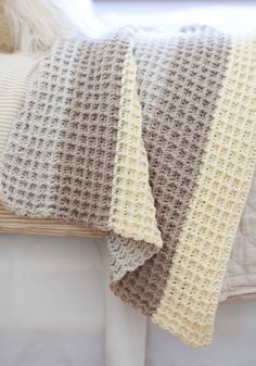 a crocheted blanket sitting on top of a white bed next to pillows and blankets