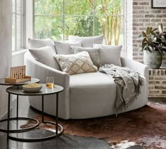 a living room filled with furniture next to a brick wall covered in plants and windows