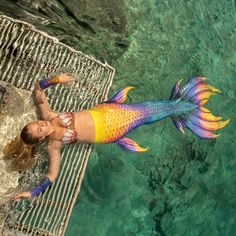 a woman in a colorful mermaid tail swims through the water with her arms outstretched