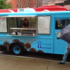 a person with an umbrella standing in front of a food truck that sells donuts