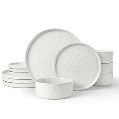 a stack of white plates and bowls on a white surface with one bowl in the middle