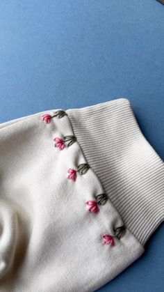 a white sweater with pink flowers is laying on a blue surface next to a pair of scissors