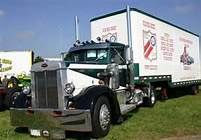 a large semi truck parked on top of a lush green field next to other trucks