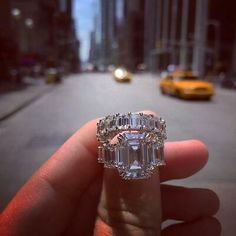 a person holding up a ring with an emerald cut diamond in the middle of it