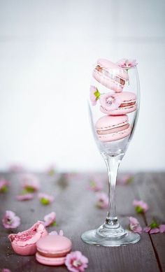 a wine glass filled with pink macaroons sitting on top of a wooden table