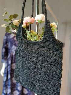 a crocheted bag with flowers in it hanging from a hook on a clothes rack