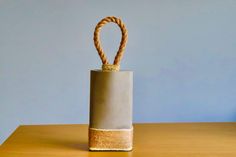 a small gray vase with a rope wrapped around it on a wooden table in front of a blue wall