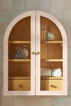 an arched wooden cabinet with towels and other items on it's shelves in a bathroom