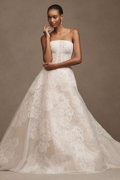 a woman in a strapless wedding dress poses for the camera with her hand on her cheek