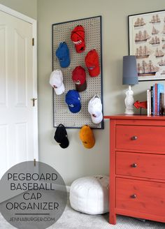 a baseball cap organizer hanging on the wall next to a red dresser and orange chest