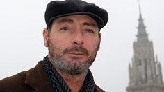 a man wearing a hat and scarf standing in front of a building with a spire