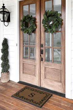 two wreaths on the front door of a white house with wood floors and windows