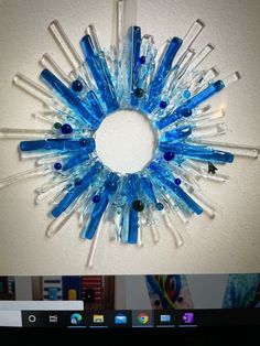 a clock made out of blue and clear glass tubes on a wall above a computer screen