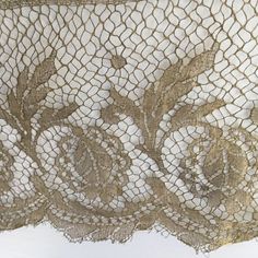 an old lace curtain is hanging on the side of a white wall with flowers and leaves