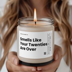 a woman holding a candle that says smells like your twenties are over