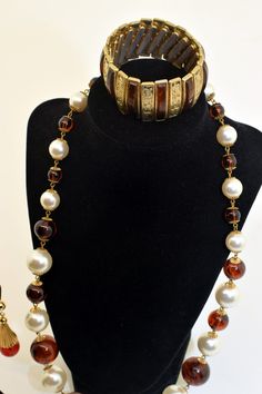 Vintage dark brown set Set includes a pair of earrings, a necklace, and a bracelet. The necklace is made up of large dark brown clear beads and white beads with gold tone metal between each bead, measuring 26 ½ inches in length from end to end. The drop clip back earrings are very art deco made in a gold tone metal with a dark brown clear bead at the bottom, measuring 2 ¼ inches in length. The bracelet has a metal elastic band with clear brown rectangle stone and gold tone metal with carved desi Luxury Vintage Brown Necklace, Clear Beads, White Beads, Gold Tone Metal, A Necklace, Elastic Band, Jewelry Sets, Dark Brown, Gold Tones