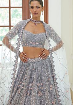 Step into elegance with this exquisite Silver Grey Bridal Lehenga Set. The silver grey satin choli is a masterpiece, embellished with shimmering silver beads, sequins, metallic accents, and sparkling crystals. Delicate 3-D rose pink florets add a touch of romance to the ensemble. The graceful silver grey net lehenga flows beautifully, while the matching net dupatta adds a final touch of sophistication. Perfect for the discerning bride who wants to make a statement on her special day. Composition : Blouse-Satin, Lehenga and Dupatta- Net Care: Dry Clean Only and Vacuum Storage This product can be customized for sleeves, length of blouse and neckline Delivery : 6-8 weeks as the product is hand crafted. Check Size Guide or choose MySize for free customisation (All Sizes above XL can be made at Grey Bridal Lehenga, Satin Lehenga, Blouse Satin, Bridal Lehenga Red, Net Lehenga, Vacuum Storage, Indian Wedding Wear, Satin Blouses, Net Dupatta