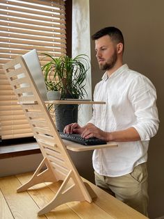 a man standing in front of a laptop computer on a wooden desk next to a plant