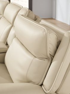 the back seats of a white leather couch in a living room with wood flooring