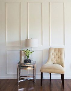 a chair and table in a room with white paneling on the wall behind it